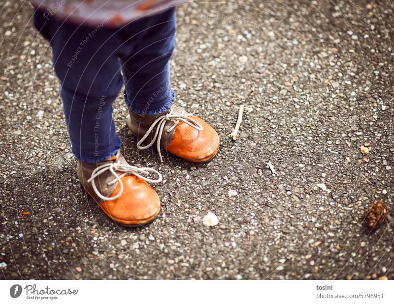 Kleinkind steht mit orangenen Schuhen auf Asphalt Kind Kindheit Schuhe zubinden stehen laufen lernen Kinderschuhe Schnürsenkel Beine Außenaufnahme gehen Straße