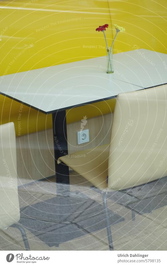 Weißer Stuhl und Tisch vor gelber Wand. Auf dem Tisch ein Glas mit einer gelben und roten Blume. Interior Farben Stil Raum Warten einsam Möbel Einrichtung