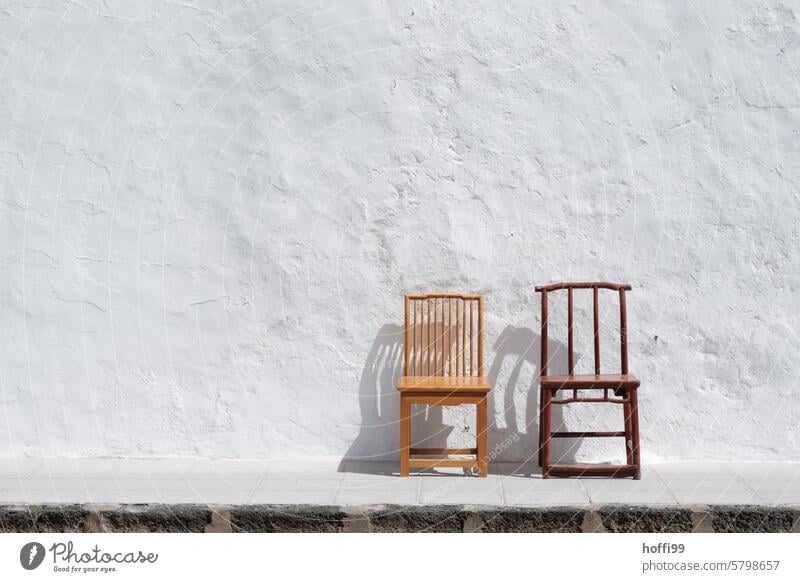 zwei leer alte Holzstühle vor einer weiß gekalkten Wand Holzstuhl weiße wand mediterran Sommer Hitzewelle heiß trocken Trockenheit Menschenleer Fassade