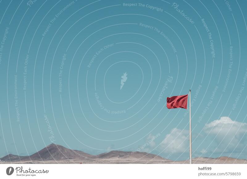 rote Fahne im Wind vor blauem Himmel und bergigem Panorama Rote Fahne Warnung Warnfarbe Achtung freigestellt minimalistisch Außenaufnahme Sicherheit Warnhinweis