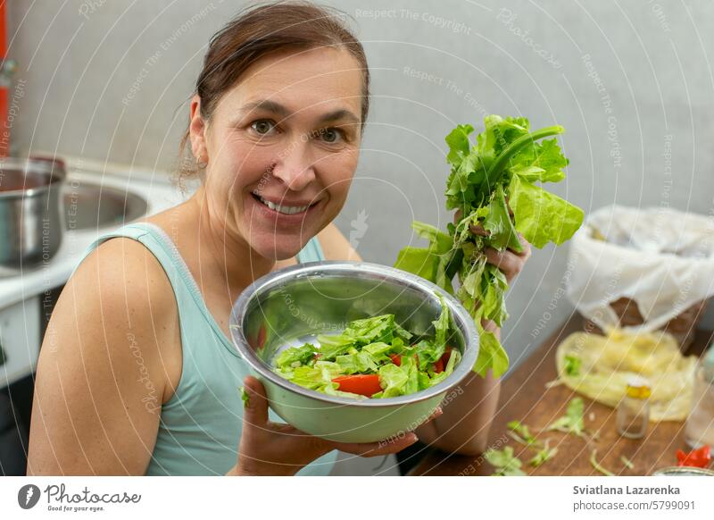 Eine Frau zeigt eine Schüssel mit Gemüse und Kräutern mit Salatblättern vor dem Hintergrund der Küche. Frauen Person Salatbeilage Lebensmittel Lifestyle