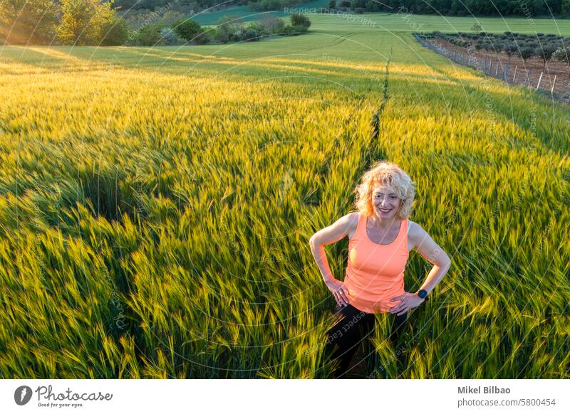 Junge kaukasische reife Frau in einem Gerstenfeld bei Sonnenuntergang.  Ayegui, Navarra, Spanien, Europa. Lifestyle-Konzept. Menschen Feld Natur Mädchen