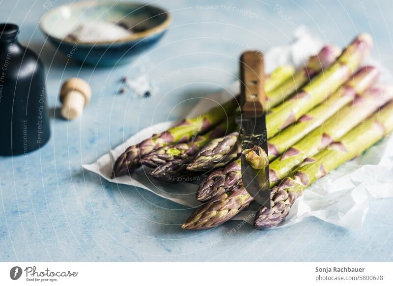Grüner Spargel und ein Messer auf einem hellblauen Tisch. Frühling, Gemüse. grün frisch roh schälen Vegetarische Ernährung Lebensmittel Diät Bioprodukte