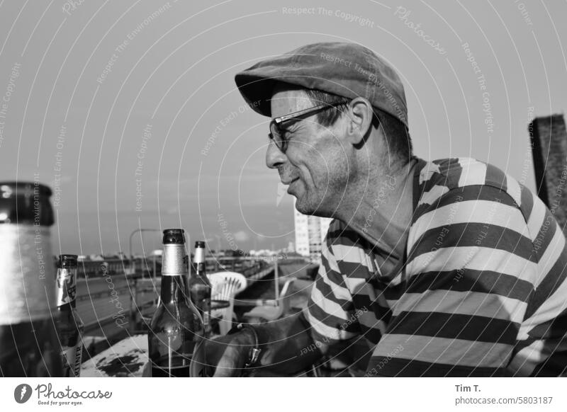 Mann mit Hut, Brille, Bier s/w Lächeln Seitenansicht Terrasse Dach Treptow Berlin Schwarzweißfoto Tag Außenaufnahme Stadt Hauptstadt Stadtzentrum bnw