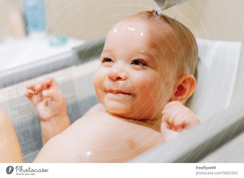 Porträt eines neun Monate alten Babys, das ein Bad nimmt und dem das Wasser durch das Gesicht läuft Badewanne Kleinkind Junge männlich Dusche Kaukasier Sitzen
