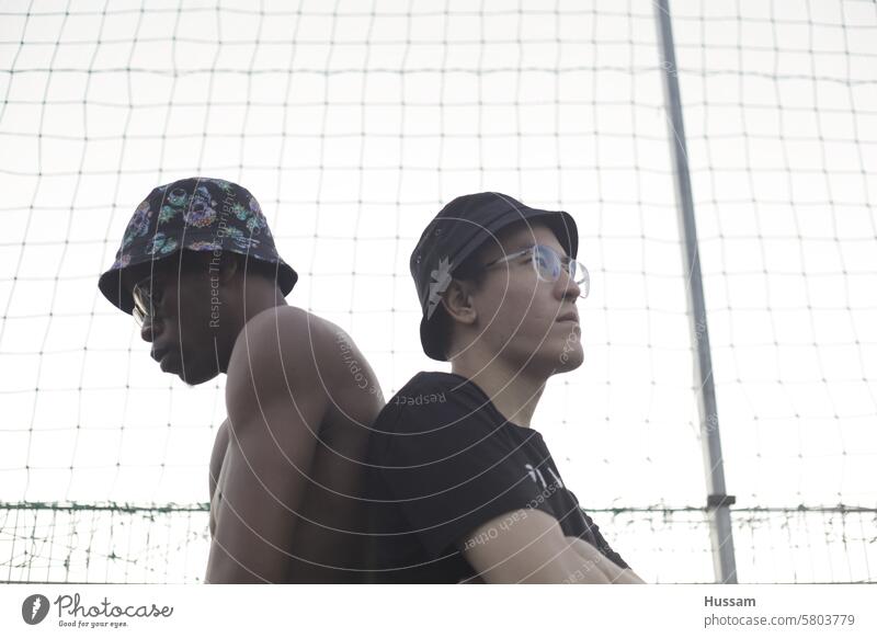 Foto von zwei Freunden, die Hüte tragen und Rücken an Rücken auf einem Spielplatz posieren Hintergrund Menschen vereinzelt Mode Natur Konzept Gesundheit Glück