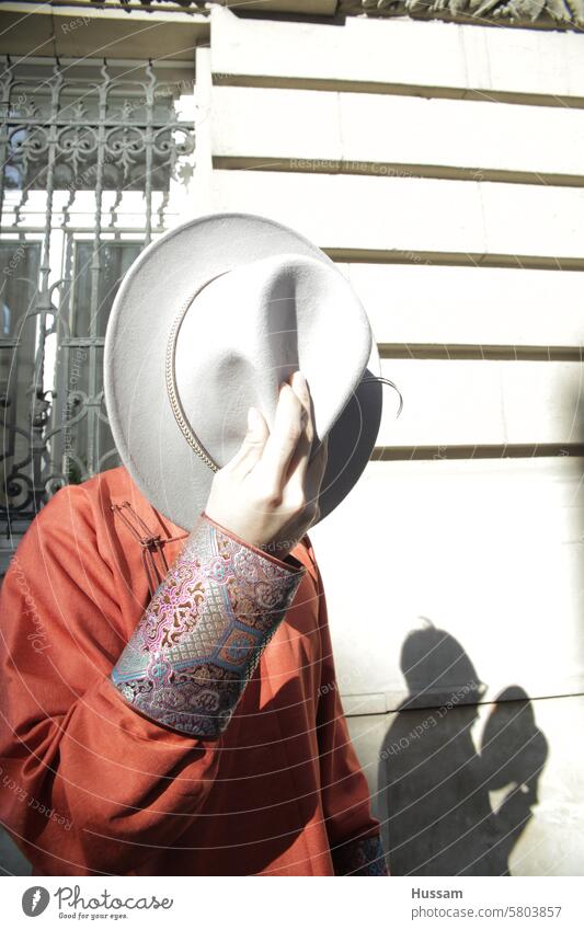 ein Foto einer anonymen Person, die einen Hut hält, der ihr Gesicht mit einem Schatten bedeckt, der sich auf einem alten Gebäude spiegelt reisen Mode Mann