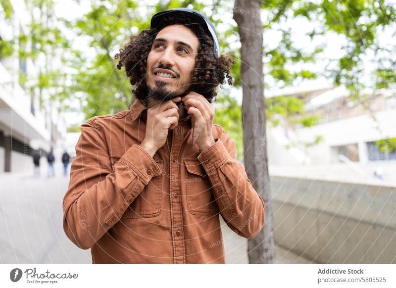 Junger Mann passt seinen Helm im Freien vor einer Stadtrundfahrt an Schutzhelm Sicherheit Mitfahrgelegenheit urban verantwortlich Genuss krause Haare jung