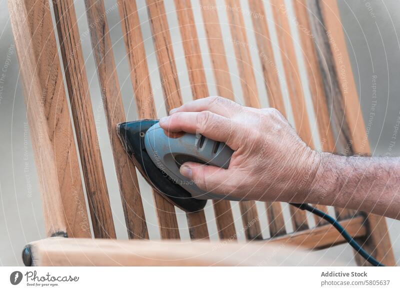 Nahaufnahme eines Mannes beim Schleifen eines Holzstuhls Hand Elektroschleifer Glättung Oberfläche Lackierung Arbeit Handarbeit Möbel Restauration