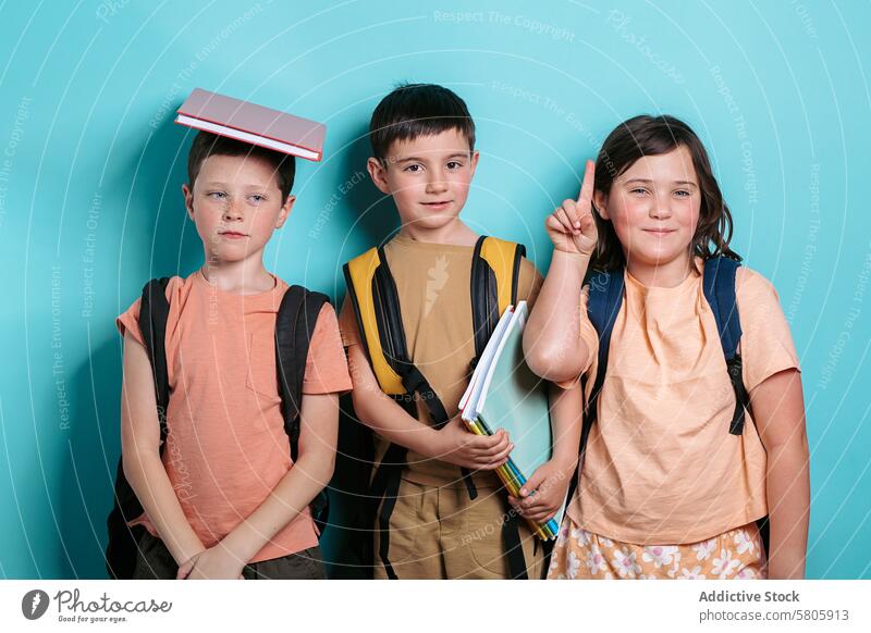Drei Schulkinder mit Rucksäcken und Büchern Schule Kinder Jungen Mädchen blau Hintergrund Bildung Lächeln in die Kamera schauen Stehen lässig Bekleidung Schüler
