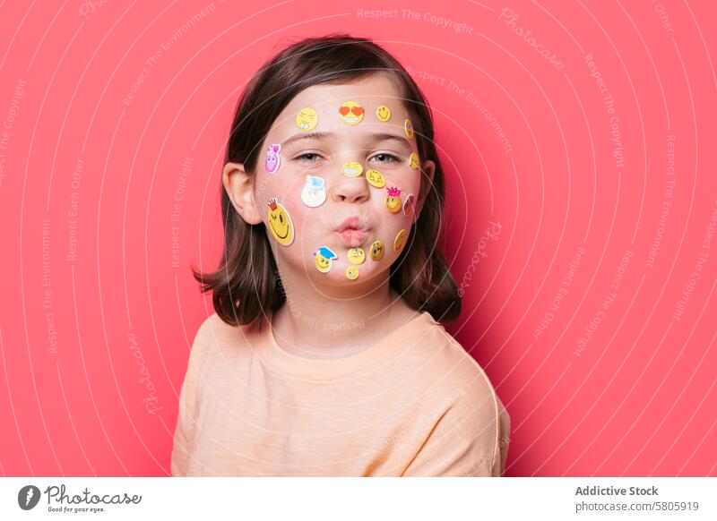 Junges Mädchen mit Emoji-Aufklebern im Gesicht macht Schmollmund Kind Dekoration & Verzierung Spaß spielerisch Ausdruck Kussmund niedlich Schulkind Emotion