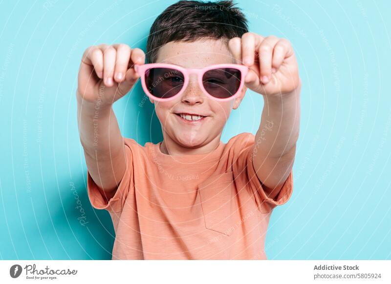 Lächelnder Schuljunge mit rosa Sonnenbrille Schulkind Junge spielerisch Blauer Hintergrund Fröhlichkeit Kindheit Brille Mode Stil heiter Accessoire Porträt