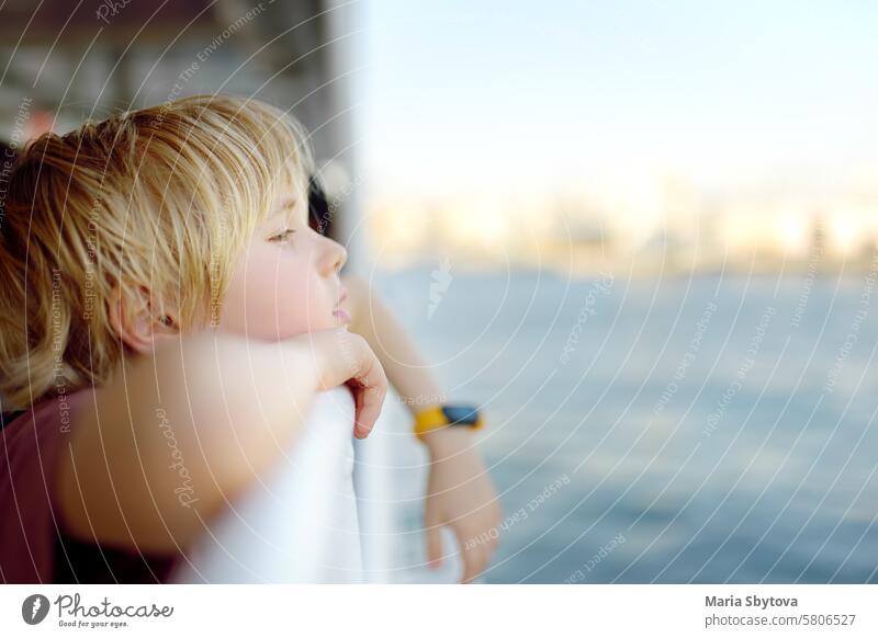 Cute blonde preteen Junge reist mit dem Boot oder Fähre auf dem Meer. Familienurlaub am Ozean oder Meer. Sommerfreizeit für Familien mit Kindern. Kind überhitzt an einem heißen sonnigen Tag.