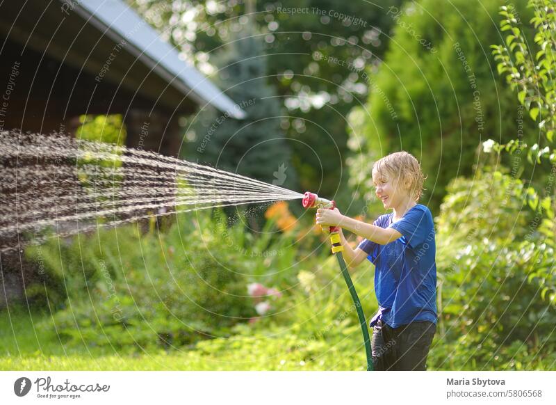 Lustiger kleiner Junge spielt mit Gartenschlauch in sonnigen Hinterhof. Preschooler Kind Spaß mit Spray von Wasser haben. Sommerferien im Dorf für Kinder.