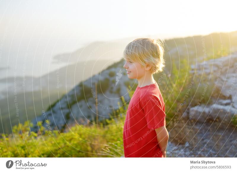 Niedlicher Junge bewundert die Aussicht auf die Budva-Riviera vom Fort Kosmach bei Sonnenuntergang. Die Ruinen der alten Festung befinden sich in den Bergen in der Nähe von Budva in Montenegro. Panoramalandschaft an der Adriaküste