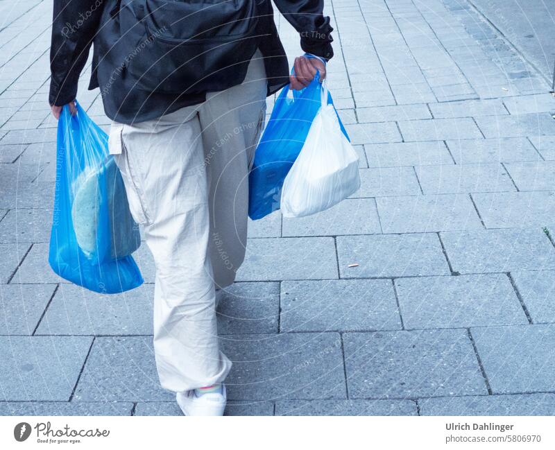 Person von hinten in weißen Hosen mit blauen und weißer Einkaufstüte.Dynamisch beim Gehen Eile Blau zielstrebig Bewegung Straße Konsum kaufen