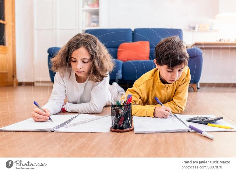 Kinder bei den Hausaufgaben auf dem Wohnzimmerboden zwei Bildung Lernen schreibend Fokus lernen Stifte Notebook Rechner Stock Konzentration im Innenbereich