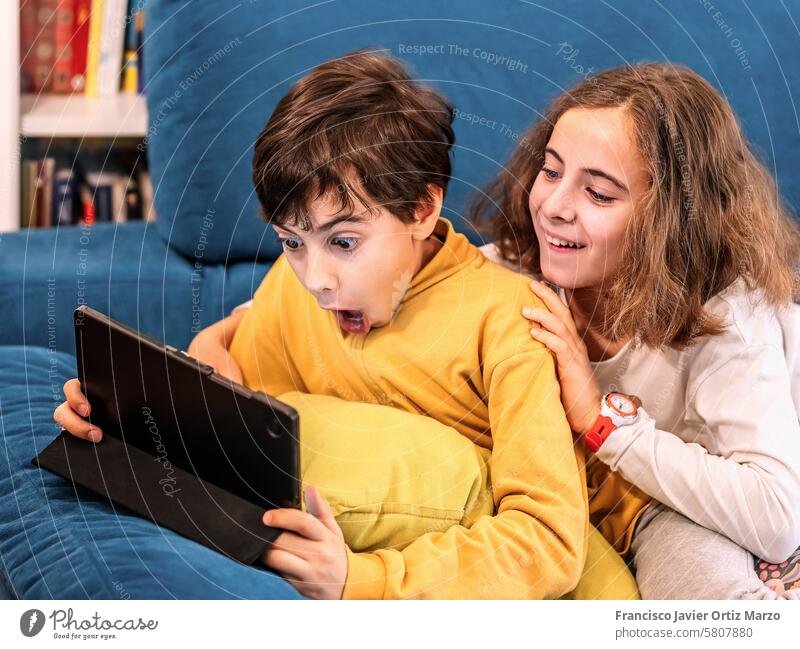 Kinder beschäftigt mit digitalem Tablet auf gemütlichem blauen Sofa zwei überrascht Tablette Technik & Technologie heimwärts im Innenbereich Lernen