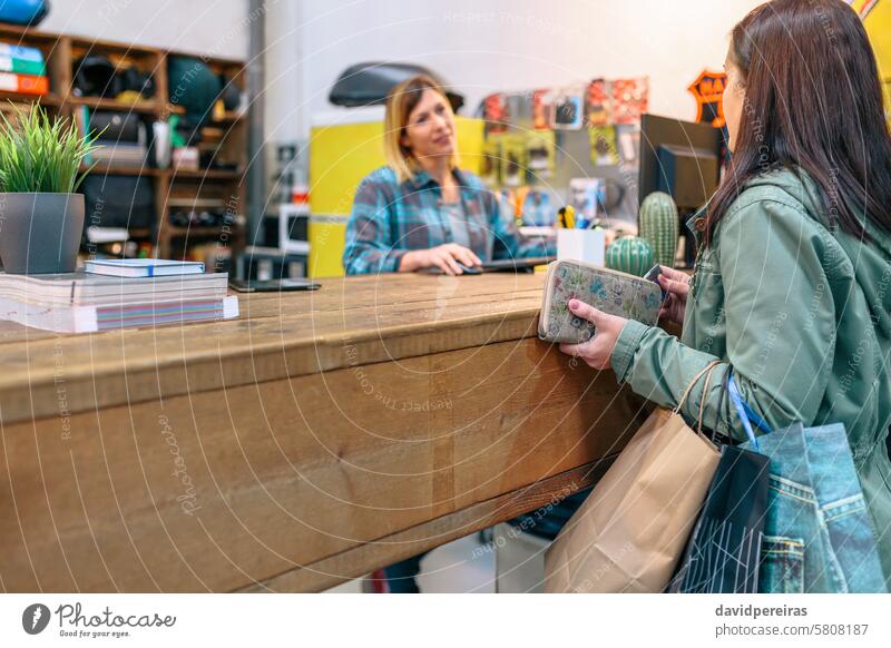 Weiblicher Kunde nimmt Kreditkarte, um gekaufte Artikel zu bezahlen, während er mit einer Mitarbeiterin im Laden spricht Klient Frau unter Postkarte Zahlung