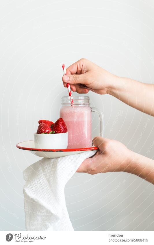 eine Hand hält einen Teller mit einem Glas Erdbeer-Smoothie auf einem weißen Hintergrund trinken Lebensmittel Frucht organisch Gesundheit Frühstück Saft Diät