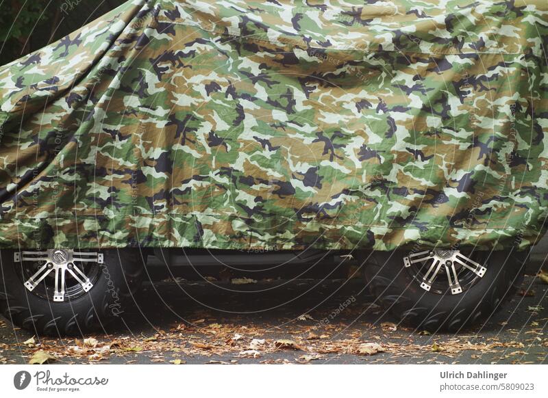 Geländefahrzeug unter Camouflagedecke.Die Räder schauen teilweise hervor. Tarnung Versteck Krieg Militär verstecken