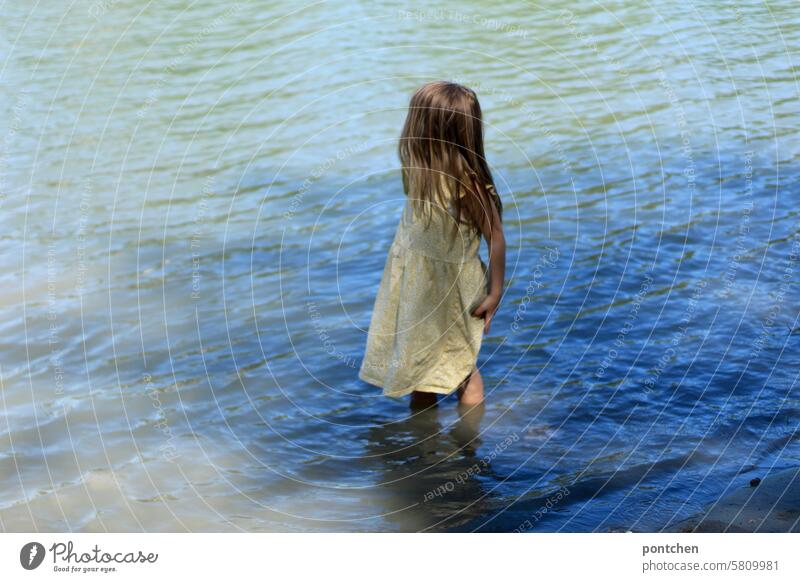 ein kind im kleid steht knöcheltief im wasser. erfrischung mädchen lange haare blau fluss inn Außenaufnahme Sommer Natur