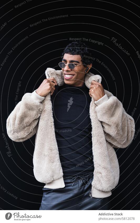 Lächelnder trendiger ethnischer Mann mit Sonnenbrille auf schwarzem Hintergrund Mode Stil maskulin heiter Individualität zuhören Musik Ohrstöpsel Porträt