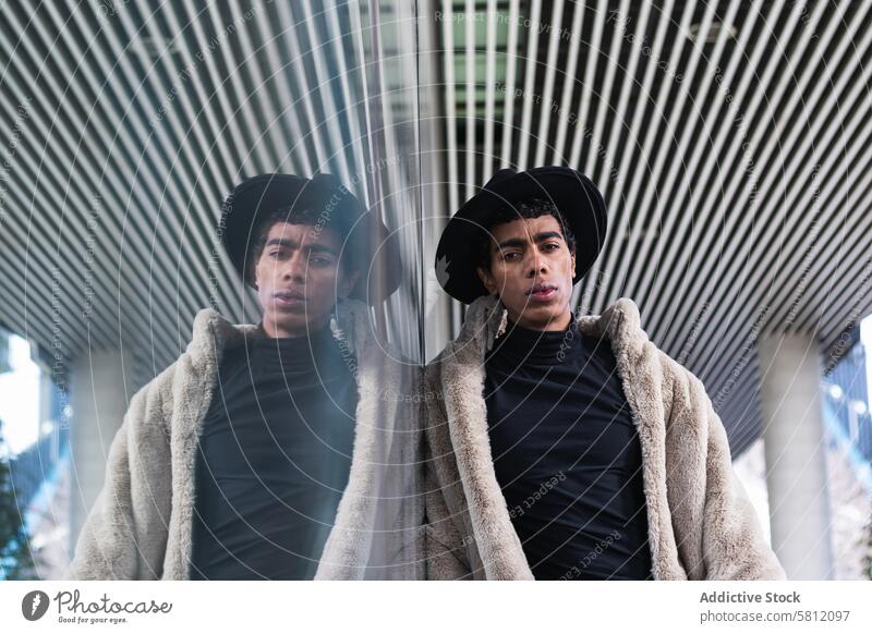 Stilvoller ethnischer Mann, der sich in einer Glaswand auf der Straße spiegelt Mode trendy Individualität Zeitgenosse Reflexion & Spiegelung Stadt Schnüffler