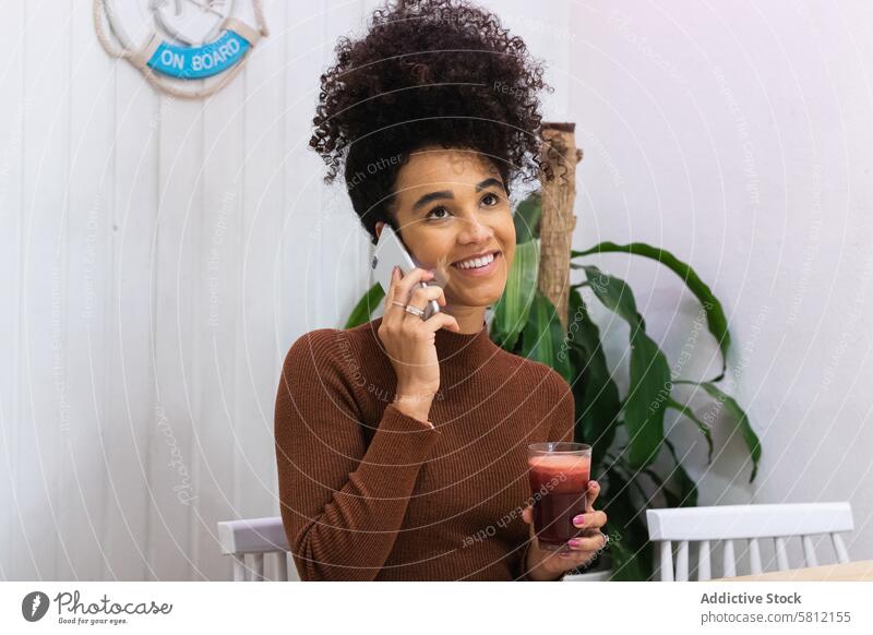 Zufriedene schwarze Frau, die in einem Café mit einem Mobiltelefon spricht Arbeit Telefonanruf freiberuflich Browsen Smartphone benutzend heiter Surfen