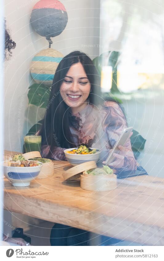 Lächelnde Frau, die in einem Restaurant isst und dabei ein Mobiltelefon benutzt Frauen Zusammensein Freund Smartphone teilen Zeit verbringen Freundschaft