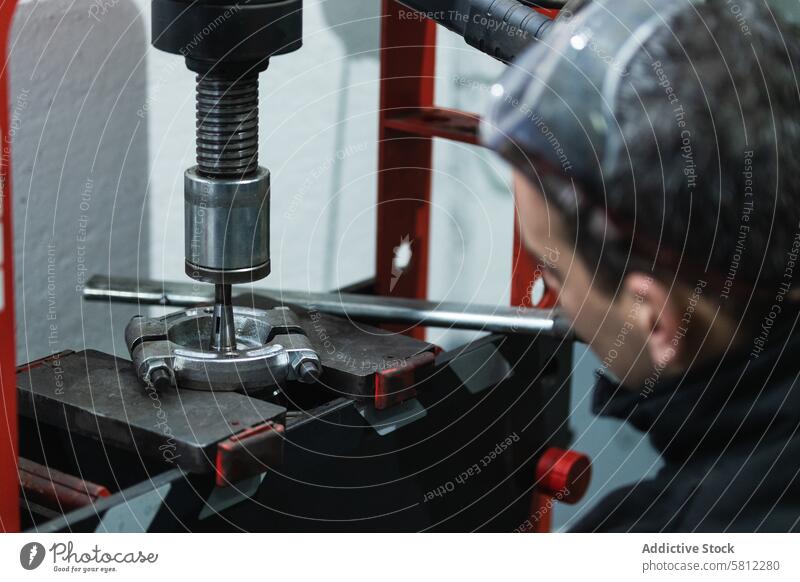 Konzentrierter Mann bei der Arbeit an einer hydraulischen Presse in einer Garage installieren Maschine Auto Mechaniker Job Fokus männlich Erwachsener