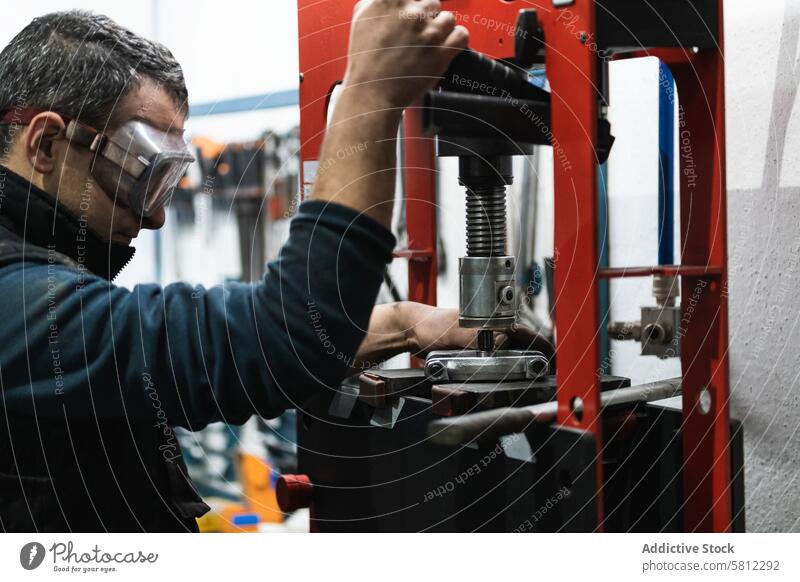 Konzentrierter Mann bei der Arbeit an einer hydraulischen Presse in einer Garage installieren Maschine Auto Mechaniker Job Fokus männlich Erwachsener