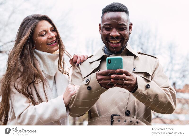 Fröhliches multiethnisches Paar benutzt Smartphone im Park benutzend Glück Zusammensein Mobile Telefon romantisch Liebe Inhalt Erwachsener rassenübergreifend