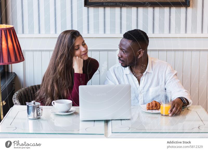 Fröhliches multiethnisches Paar benutzt Laptop beim Frühstück zu Hause benutzend Zusammensein Glück Partnerschaft heiter Browsen zuschauen rassenübergreifend