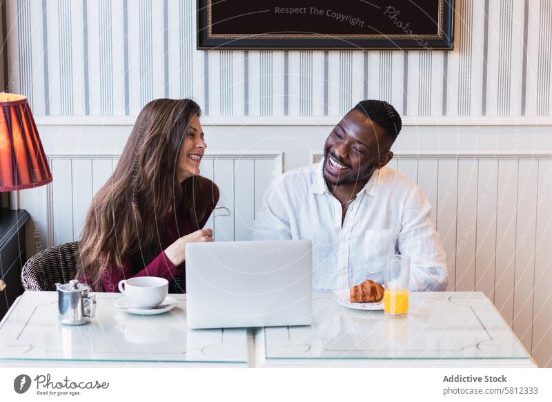 Fröhliches multiethnisches Paar benutzt Laptop beim Frühstück zu Hause benutzend Zusammensein Glück Partnerschaft heiter Browsen zuschauen rassenübergreifend