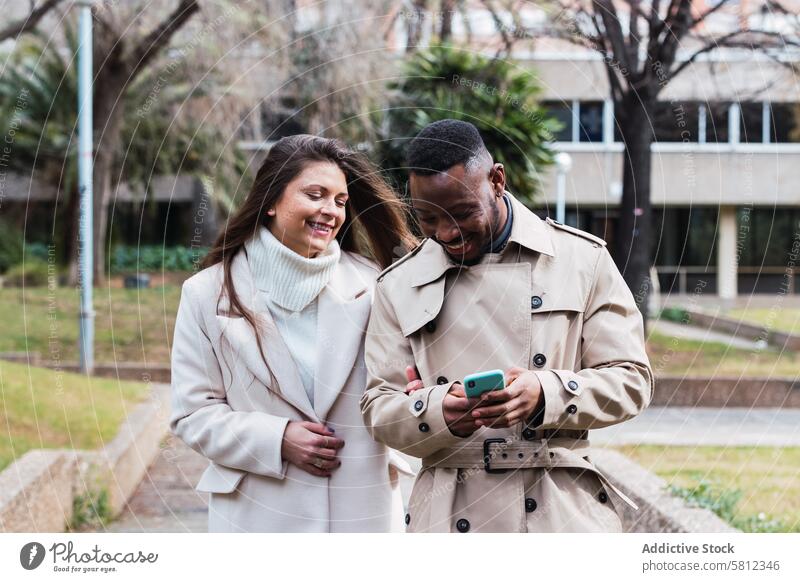 Fröhliches multiethnisches Paar benutzt Smartphone im Park benutzend Glück Zusammensein Mobile Telefon romantisch Liebe Inhalt Erwachsener rassenübergreifend