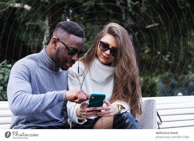 Fröhliches multiethnisches Paar hört im Park Musik auf dem Smartphone hören benutzend Glück Zusammensein Mobile Telefon romantisch Liebe Erwachsener