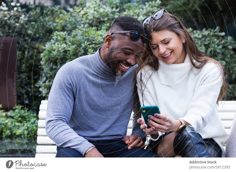 Fröhliches multiethnisches Paar hört im Park Musik auf dem Smartphone hören benutzend Glück Zusammensein Mobile Telefon romantisch Liebe Erwachsener