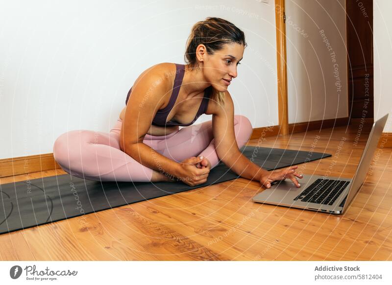 Frau in Sportkleidung macht Yoga mit Laptop zu Hause Gesundheit Übung Lifestyle Fitness heimwärts Körper Training Kaukasier Sportbekleidung Pilates jung Stock