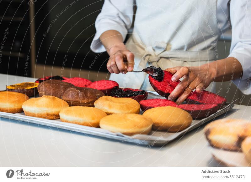 Erntekoch beim Auftragen von Marmelade auf Biskuitkuchen in der Backstube Bäcker Schwamm Kuchen hinzufügen Aufstrich Veganer Dessert Schliere Koch Küche