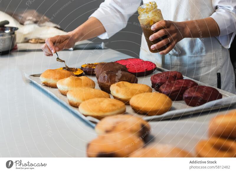Erntekoch beim Auftragen von Marmelade auf Biskuitkuchen in der Backstube Bäcker Schwamm Kuchen hinzufügen Aufstrich Veganer Dessert Schliere Koch Küche