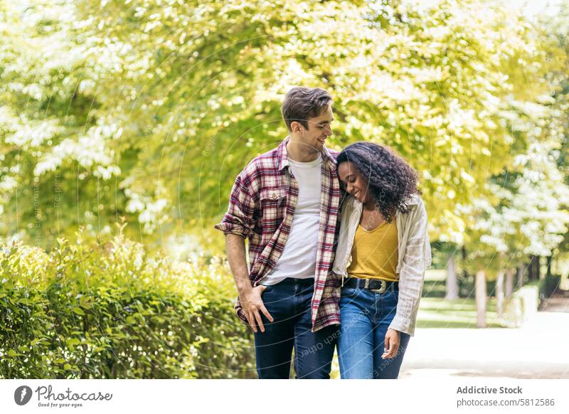 Glückliches gemischtrassiges Paar bei einem Spaziergang im Park im Freien rassenübergreifend Smartphone Lifestyle Zusammensein jung Menschen multiethnisch Spaß