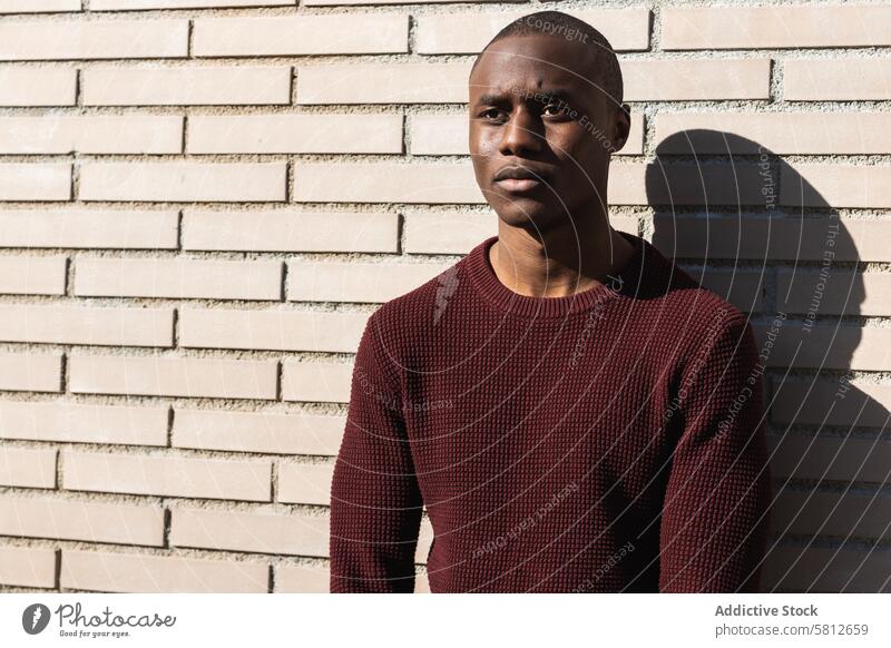 Junger Afroamerikaner, stehend in der Nähe der Quartierwand Mann lässig ernst Stil maskulin nachdenken Schatten Backsteinwand Stadt allein schwarz gestrickt