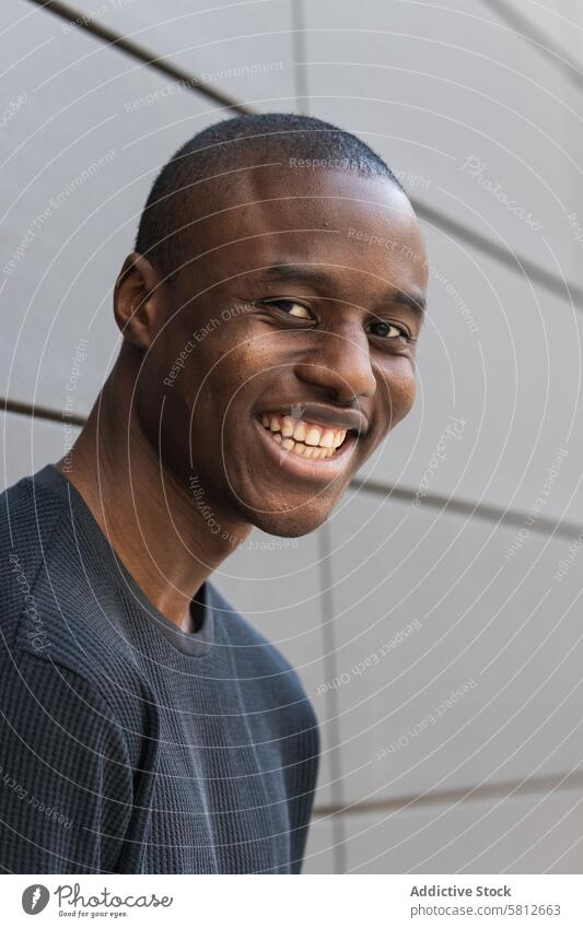 Glücklicher junger Afroamerikaner in der Nähe der Wand stehend Mann lässig Stil maskulin nachdenken Stadt allein schwarz gestrickt Kleidungsstück Jeansstoff