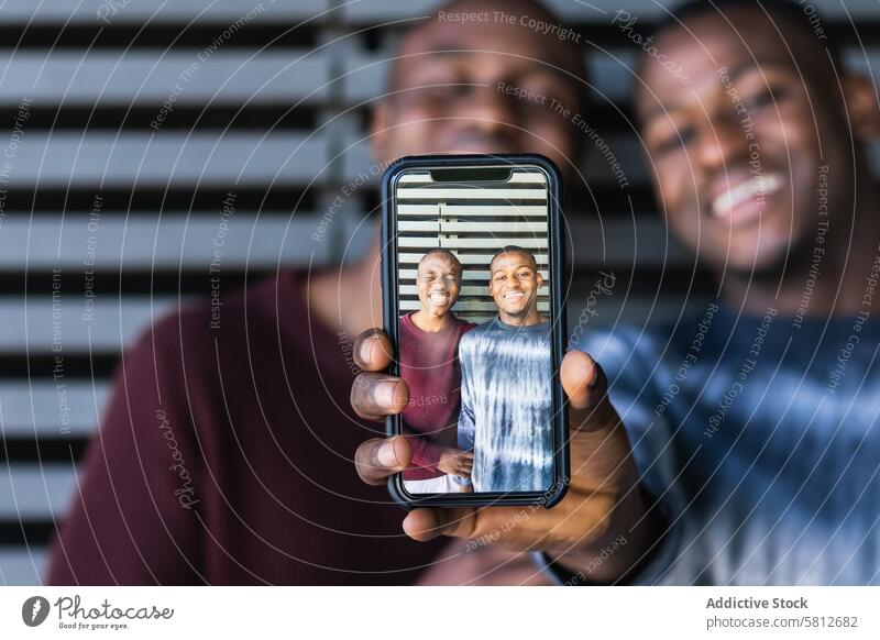 Foto auf Smartphone von schwarzen Freunden zeigen Person Männer bester Freund benutzend positiv fotografieren heiter Zusammensein sorgenfrei männlich