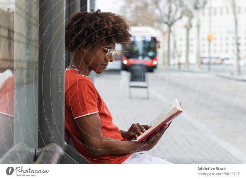 Ruhiger junger schwarzer Mann, der an der Bushaltestelle einen Roman liest lesen Buch Straße Großstadt sich[Akk] entspannen trendy tausendjährig warten urban