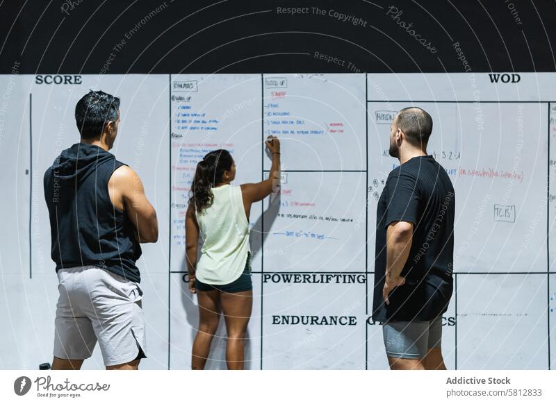Gruppe von gesichtslosen Sportlern in der Nähe der Wand mit den Ergebnissen Menschengruppe Fitnessstudio Whiteboard schreiben punkten Kraftdreikampf Training