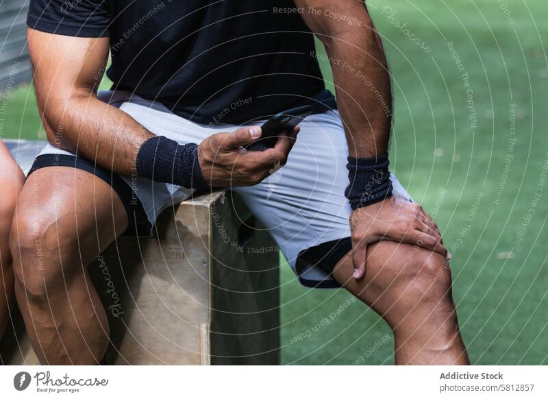 Anonymer fitter ethnischer Mann, der während des Trainings auf seinem Smartphone surft Sportler benutzend Pause Fitness Internet online sportlich zuschauen
