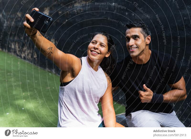 Lächelndes ethnisches Paar, das während des Trainings ein Selfie mit dem Smartphone macht Sportlerin benutzend Daumen hoch gestikulieren Pause positiv Frau Mann