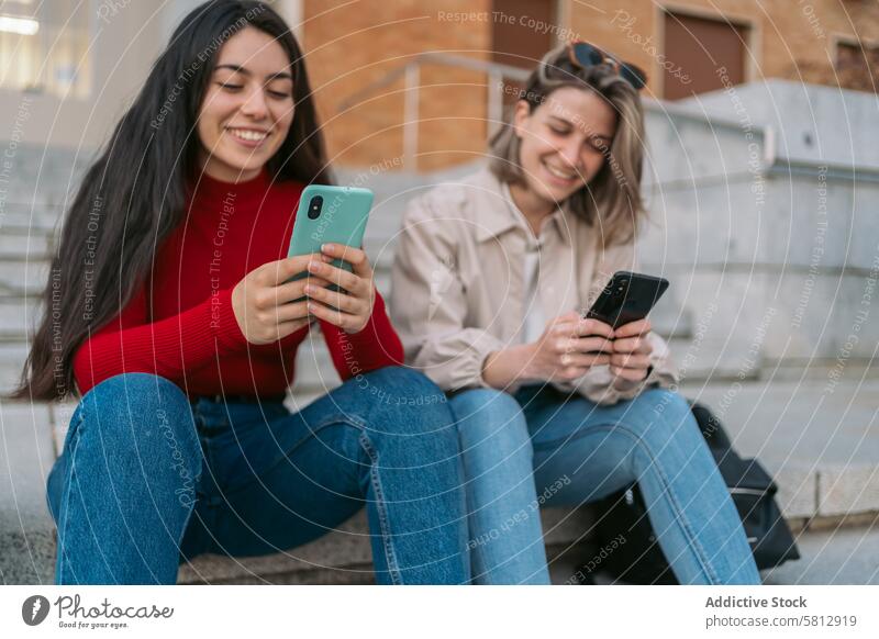 zwei Studentinnen sitzen auf der Treppe und beobachten das Handy jung Freunde Telefon Mobile Mädchen Frau Internet Schüler Menschen Paar Smartphone Glück